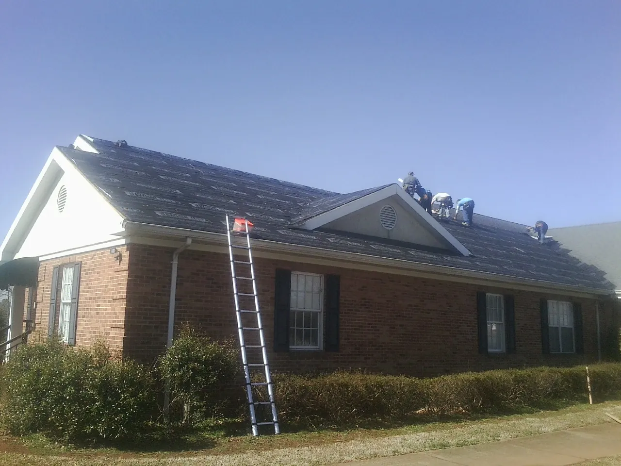 Crew tearing shingles off a brick ranch roof with a ladder set — Metal Roof Repair work by our crew in Lane