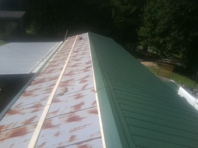 Old rusted panels beside newly installed green metal roofing — Wind Damage Roof Repair by Roofing Brothers in Lane