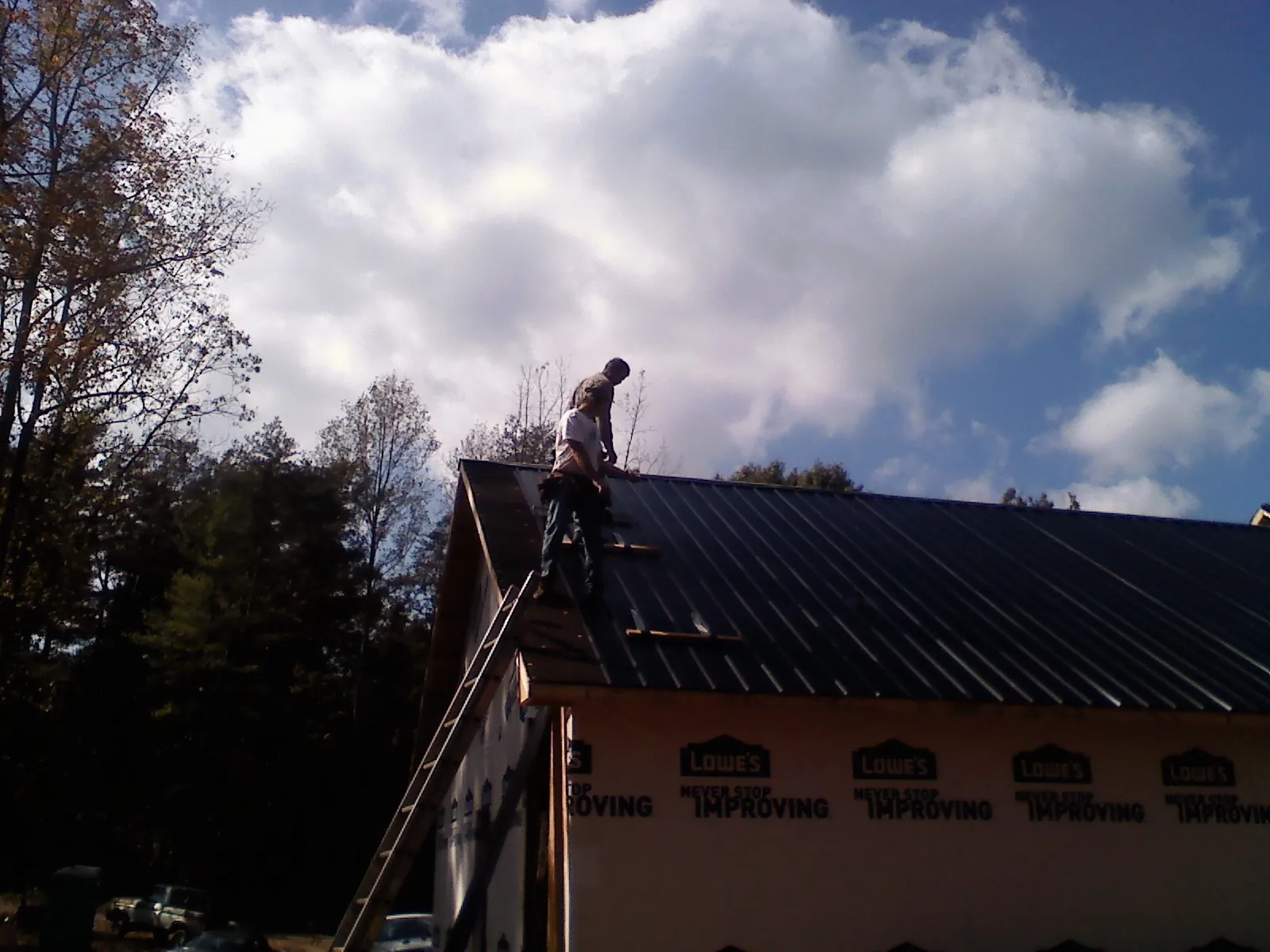 Roofer fastening dark metal panels high against a cloudy sky, from a Roof Inspection job in Lane